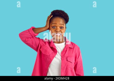 Confuso e perplesso giovane afroamericana in giacca rosa su sfondo blu. Foto Stock