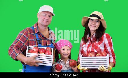 ritratto della famiglia contadina , tenendo in mano scatole di legno con mele biologiche rosse mature, sorridente, su sfondo verde in studio. Cibo sano al vostro tavolo. Foto di alta qualità Foto Stock