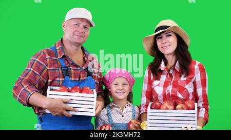 ritratto della famiglia contadina , tenendo in mano scatole di legno con mele biologiche rosse mature, sorridente, su sfondo verde in studio. Cibo sano al vostro tavolo. Foto di alta qualità Foto Stock