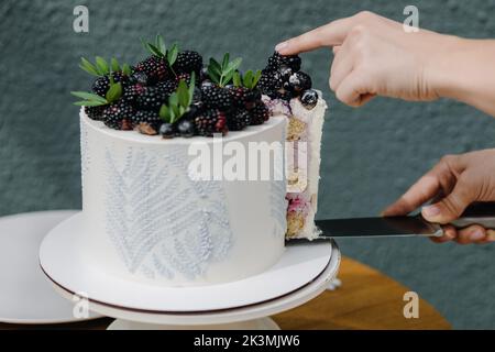 Le mani femminili tagliano a pezzi una torta fatta in casa ricoperta di frutti di bosco per servire Foto Stock