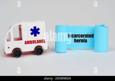 Concetto medico. Su una superficie bianca, un'ambulanza e un segno di carta blu con l'iscrizione - ernia incarcerata Foto Stock