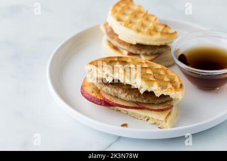 Un sandwich con waffle e salsiccia tostato servito con sciroppo d'acero per l'immersione. Foto Stock