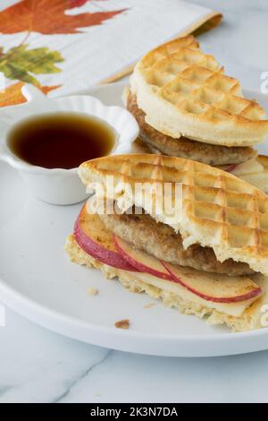 Un primo piano con waffle tostati e panini con salsiccia serviti con sciroppo d'acero. Foto Stock