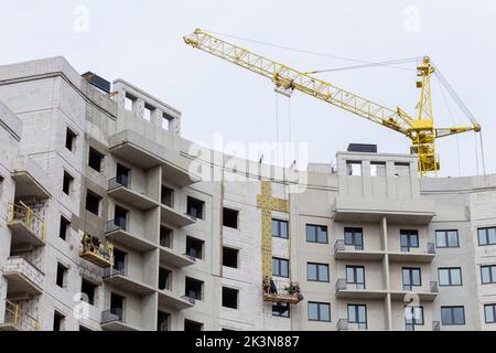 Processo di isolamento delle pareti esterne in un edificio a più piani in costruzione. I lavoratori in una culla arancione da costruzione attaccano le lana minerale Foto Stock