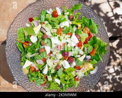 Vista dall'alto di una colorata insalata estiva con lattuga verde, pomodori, feta, cipolle, olive, ed erbe su un piatto grande dell'insalata. Foto Stock