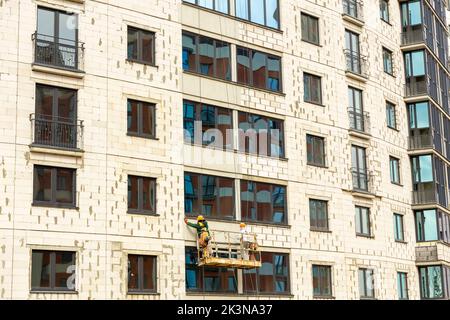 Processo di isolamento delle pareti esterne in un edificio a più piani in costruzione. I lavoratori in una culla arancione da costruzione attaccano le lana minerale Foto Stock