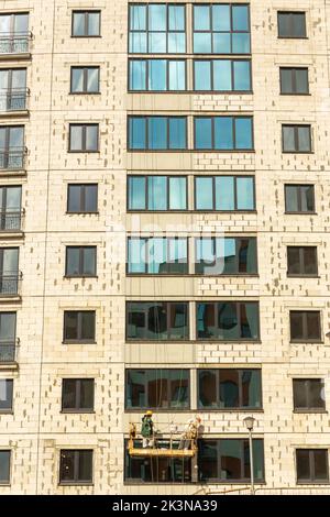 Processo di isolamento delle pareti esterne in un edificio a più piani in costruzione. I lavoratori in una culla arancione da costruzione attaccano le lana minerale Foto Stock