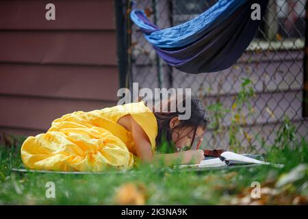 Una bambina in un abito giallo brillante giace in disegno d'erba Foto Stock