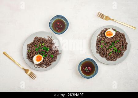 Tagliatelle Soba con uovo, cipolla verde e salsa piccante su tavola bianca. Cibo asiatico. Vista dall'alto, disposizione piatta. Foto Stock