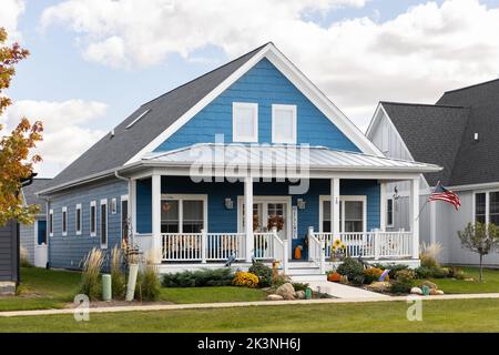 Una grande casa colonica a due piani con un vivace lato blu e un portico frontale coperto bianco. Foto Stock