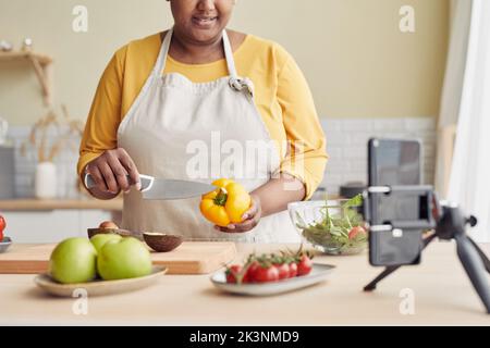 Primo piano di giovane donna nera che cucina pasto sano in cucina e registrare video con smartphone, spazio copia Foto Stock