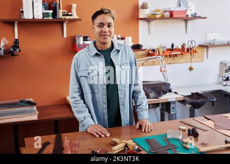 Ritratto di artigiana multietnica in officina sorridendo alla fotocamera fiero di successo piccola impresa Foto Stock