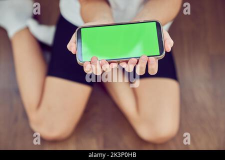 Primo piano delle mani dei bambini utilizzando un telefono con schermo verde. Una bambina è seduta sul pavimento e tiene in mano uno smartphone con un tasto colorato. Foto di alta qualità Foto Stock