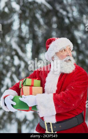 Vita in su ritratto di Babbo Natale tradizionale portare regali all'aperto nella foresta invernale e guardare cauto Foto Stock