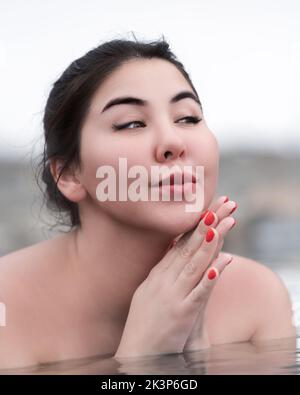 Ritratto di donna giocosa con palme ripiegate sotto il mento e guardando lontano. Autentico plump brunette modello bagno e relax in acqua minerale di spa Foto Stock