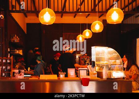 Bangkok, Thailandia - 23 gennaio 2022: Personale impegnato a preparare bevande e caffè da servire al cliente all'interno di un negozio locale decorato da luce arancione brillante Foto Stock