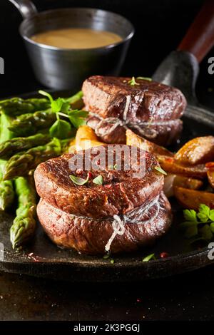 Gustosi medaglioni di manzo con asparagi e patate serviti su padella vicino alla pentola con salsa durante la cena Foto Stock