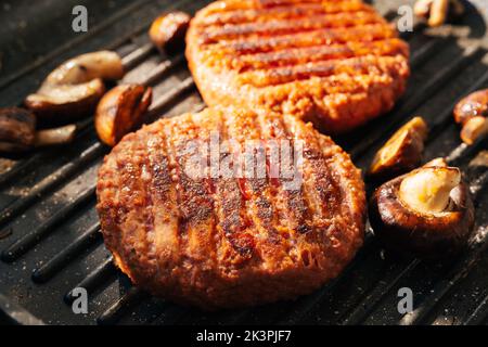 Polpettine di hamburger Pilz sfrigolando su una padella calda barbecue con funghi. Cibo vegano. Primo piano Foto Stock