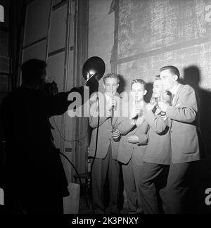 1950s talenti. Un gruppo di quattro giovani sta entrando in uno spettacolo di talenti con la loro performance di fare musica soffiare in bottiglie di Coca Cola. Dato che le bottiglie sono riempite con diversi livelli di acqua, fanno suoni diversi quando soffiano sopra di loro, abbastanza sembra fare un pezzo musicale abbastanza lungo da eseguire con. Nota il trucco dei fotografi di utilizzare le luci di un altro fotografi. Svezia 1954 Kristoffersson Ref BX37-12 Foto Stock