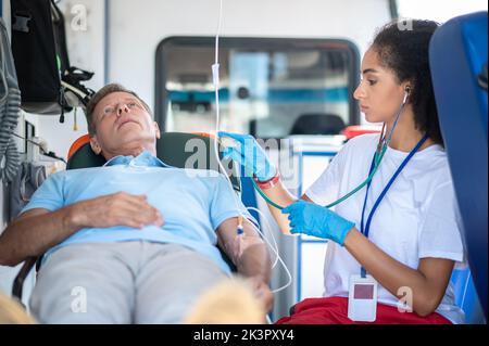 Donna focalizzata paramedica auscultante il paziente maschile Foto Stock