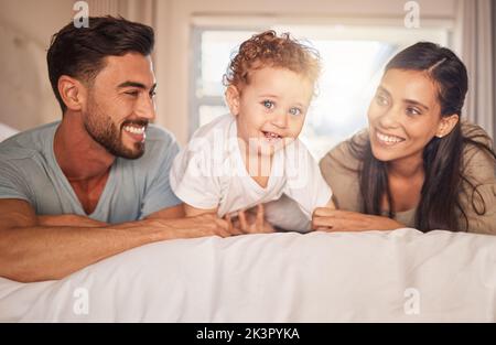 Felice, amore e genitori con il loro bambino a letto in camera da letto legame, giocare e rilassarsi a casa. Felicità, sorriso e coppia che si posa con loro Foto Stock