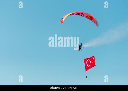 Smirne, Turchia - 9 settembre 2022: Jumper paramotore sul cielo con un'enorme bandiera turca nel giorno della libertà di Smirne a Izmir Konak Turchia Foto Stock