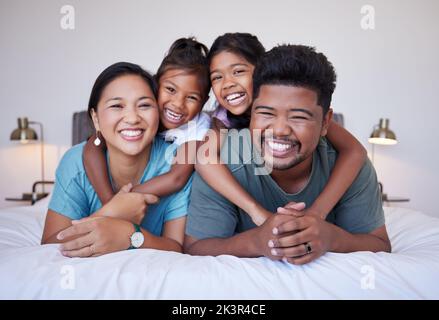 Ritratto di una felice famiglia asiatica sul letto con un sorriso sul viso. Famiglia indiana multiculturale nella loro camera da letto sorridendo, ridendo e divertendosi Foto Stock