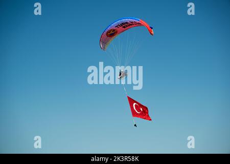 Smirne, Turchia - 9 settembre 2022: Jumper paramotore sul cielo con un'enorme bandiera turca nel giorno della libertà di Smirne a Izmir Konak Turchia Foto Stock