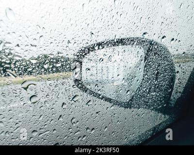 Specchio per auto e finestrino laterale coperto da gocce di pioggia durante la pioggia d'estate pioggia doccia tempesta, messa a fuoco selettiva Foto Stock