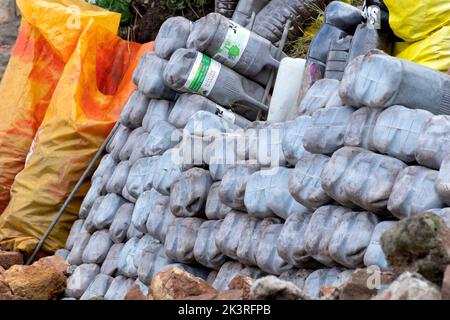 Una parete di ritegno del giardino fatta da contenitori di latte di plastica riciclati, quattro pinta, riempiti di sabbia. I mattoni Eco fanno un gabion di ritegno efficace Foto Stock