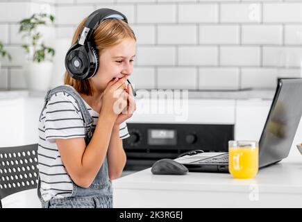 Bambina che indossa le cuffie studia con il portatile durante una lezione online a casa al coronavirus pandemico. Bambino pupilla sorridendo facendo videochiamata con o. Foto Stock