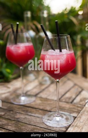 cocktail rosso con ghiaccio in vetro con gambo su superficie di legno Foto Stock