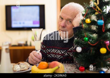 Un uomo arrabbiato ederly seduto da solo a casa a tavola a Natale Foto Stock