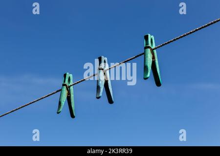 Tre clothespins di plastica appesi su un clothesline contro un cielo blu. Foto Stock