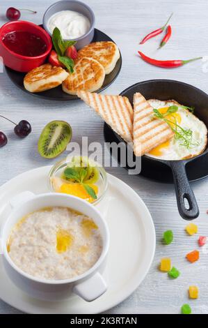 porridge con frutta, uova strapazzate, cheesecake. Concetto gustoso prima colazione Foto Stock