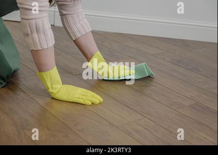 Una mano in un guanto di protezione in gomma pulisce le piastrelle con un panno in microfibra. Pulizia manuale del pavimento in parquet con una spugna. Foto Stock