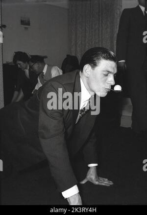 1956, storica Gran Bretagna del dopoguerra e un gentiluomo ben vestito che partecipa a una partita di festa, sul pavimento con le mani e le ginocchia con un cucchiaio in bocca bilanciando una palla, Inghilterra, Regno Unito. Foto Stock