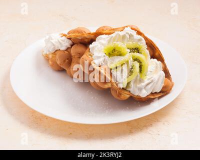 Gustosi waffle Hong Kong con kiwi e panna montata su un piatto bianco Foto Stock