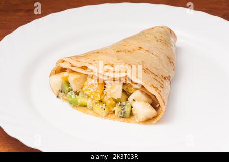 crepe gustosa con banana, arancia e kiwi su un piatto bianco Foto Stock