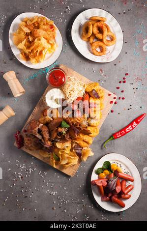 gustosi snack assortiti di birra: patatine, salsicce, anelli di cipolla, pepite di pollo, crostini, costolette affumicate, ali di pollo, salsa di pomodoro e aglio Foto Stock