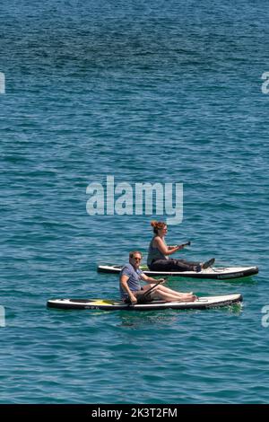 Due vacanzieri seduti su stand Up Paddleboards a Newquay Bay in Cornovaglia in Inghilterra nel Regno Unito. Foto Stock