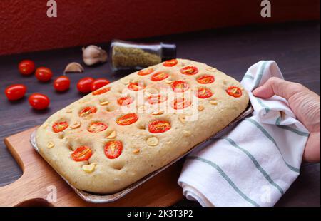 Mano dell'uomo mettere una padella di pomodoro italiano appena sfornato e focaccia all'aglio su una tavola da lettura in legno Foto Stock