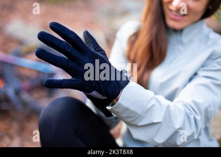 Crop donna sorridente e mettere su guanto di protezione durante il ciclismo nella campagna autunnale Foto Stock