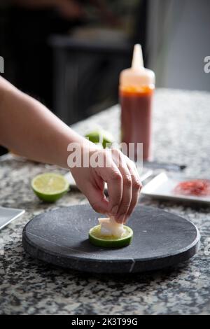 Cuoco femminile corto irriconoscibile mettendo il daikon bianco sulla fetta di lime posta sul piatto di marmo mentre cucinano nella cucina del ristorante Foto Stock