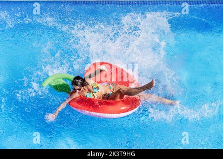 Dall'alto donna che prende il sole sull'anello gonfiabile e che spruzza in piscina Foto Stock