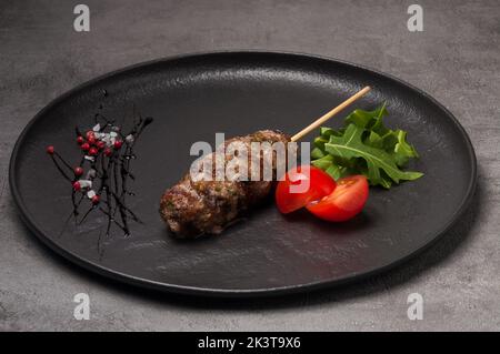 griglia porzionata lula kebab su un piatto scuro decorato con rucola e pomodori ciliegini Foto Stock