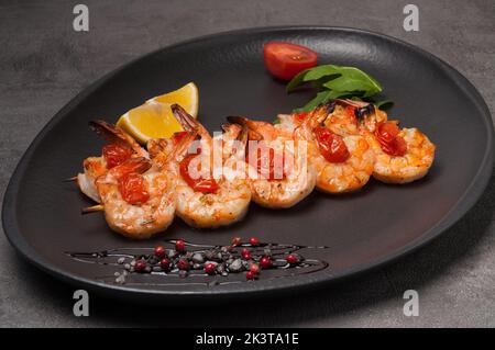 gustosi gamberetti grigliati su spiedino con pomodori su piatto scuro Foto Stock