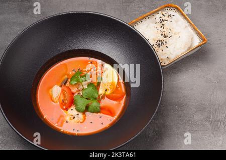 gustoso tom yam con pesce in un piatto scuro e riso Foto Stock