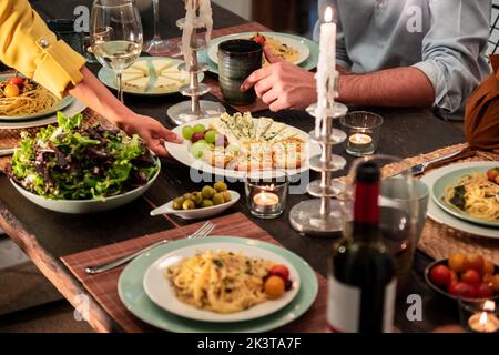 Raccoglitrice di amici intorno al tavolo festivo servito con deliziosi spuntini fatti in casa e pasta con vino durante la festa di casa Foto Stock