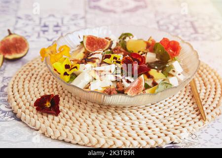 Insalata estetica francese vegetariana con feta di mango, fiori commestibili, fichi, pesca, basilico su fondo in ceramica. Cibo sano. Foto Stock